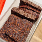 Container with slices of brown chocolate banana slice flecked with oats.