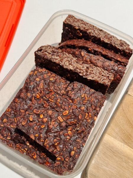 Container with slices of brown chocolate banana slice flecked with oats.